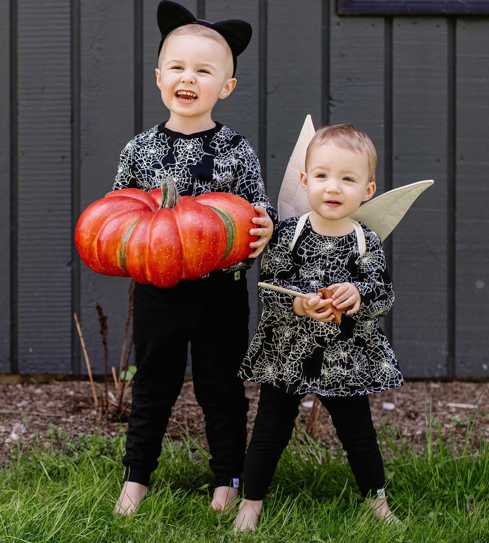 Sibling wearing matching spiderweb print outfits from Burt's Bees Baby holding orange pumpkin