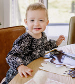 Load image into Gallery viewer, Baby girl sitting at a table wearing spiderwebs print dress from Burt&#39;s Bees Baby
