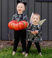 Sibling wearing matching spiderweb print outfits from Burt's Bees Baby holding orange pumpkin